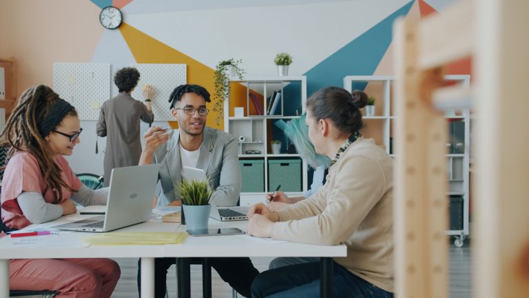 Diverse group collaborating in a bright, modern office environment with laptops and plants