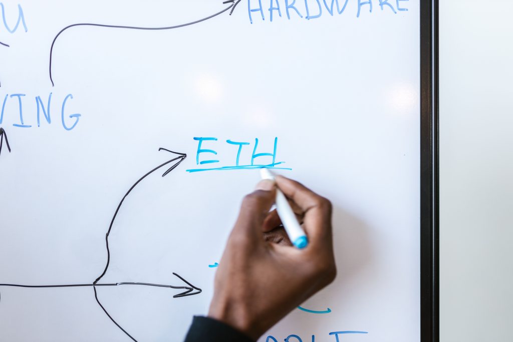 Hand writing 'ETH' on a whiteboard, highlighting Ethereum concept