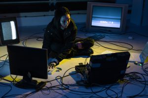 Asian woman working on multiple devices in a tech-heavy environment, illuminated by screen light