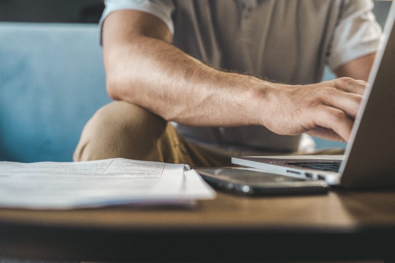 Person using a laptop beside printed documents