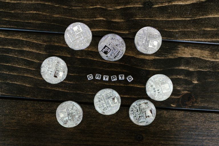 Silver cryptocurrency coins arranged on a wooden surface spelling 'crypto'