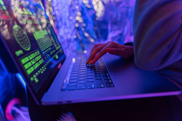 Close-up of hands typing on a laptop displaying cybersecurity graphics, illuminated by purple light