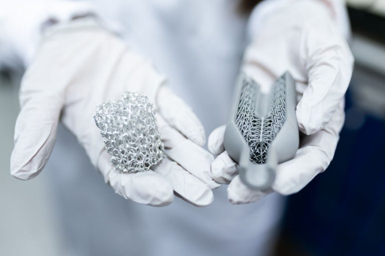 Laboratory setting showing gloved hands holding innovative 3D printed metal structures