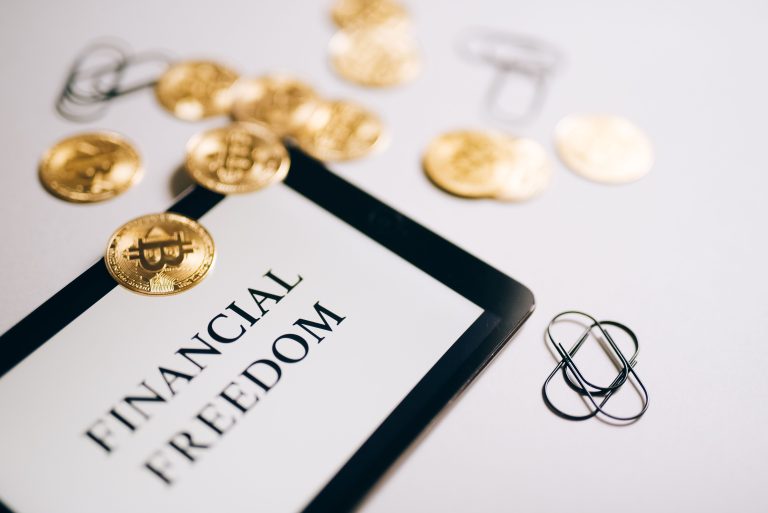 Close-up of Bitcoin coins and an iPad displaying 'Financial Freedom,' symbolizing modern digital savings