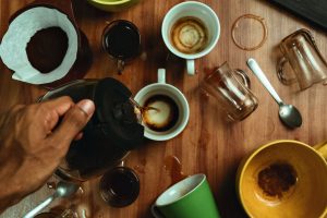 Top view of a hand pouring coffee into assorted mugs on a wooden table