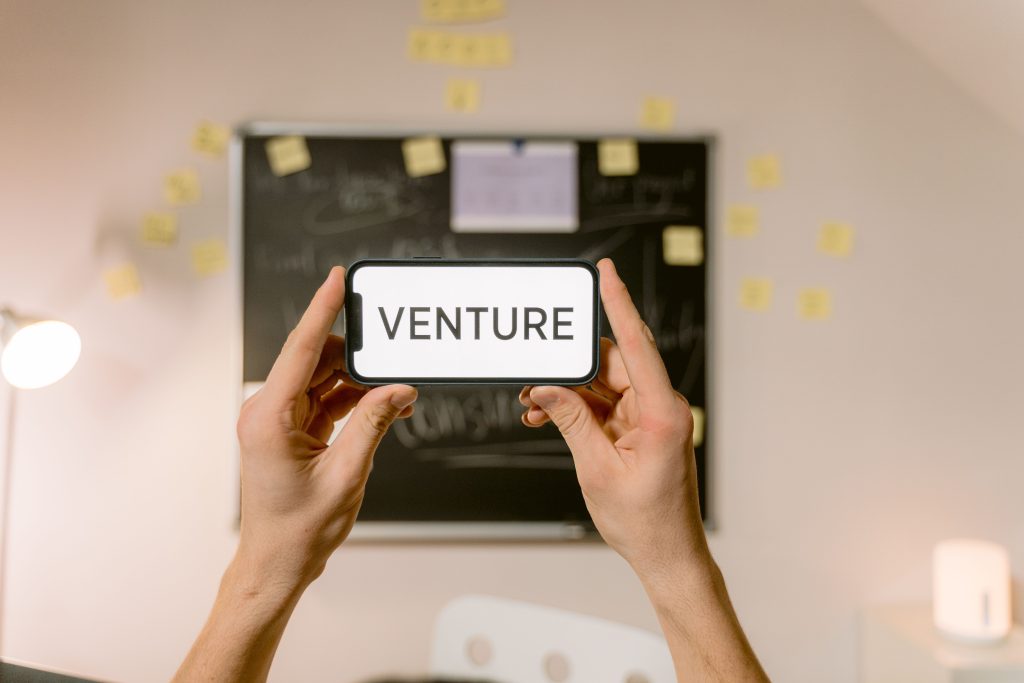 A smartphone displaying 'Venture' held by hands in an office setup